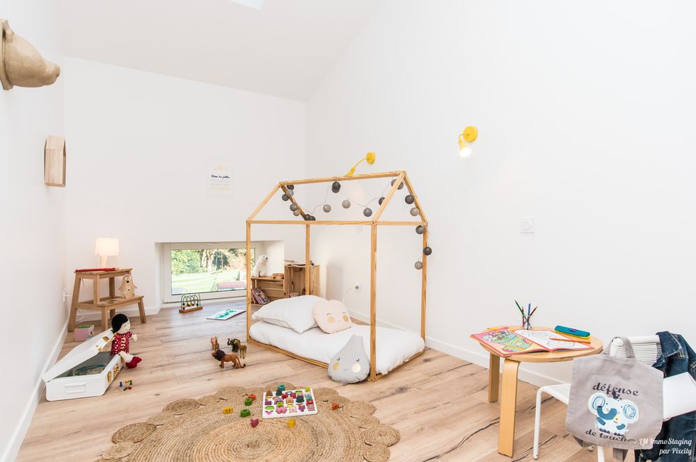 Chambre d'enfant mise en valeur par Magalie Lala : lit cabane en bois, tapis rond et jouets rangés